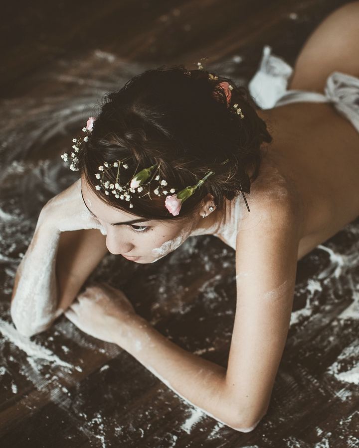 Woman lying on a flour-dusted wooden floor with flowers in her hair