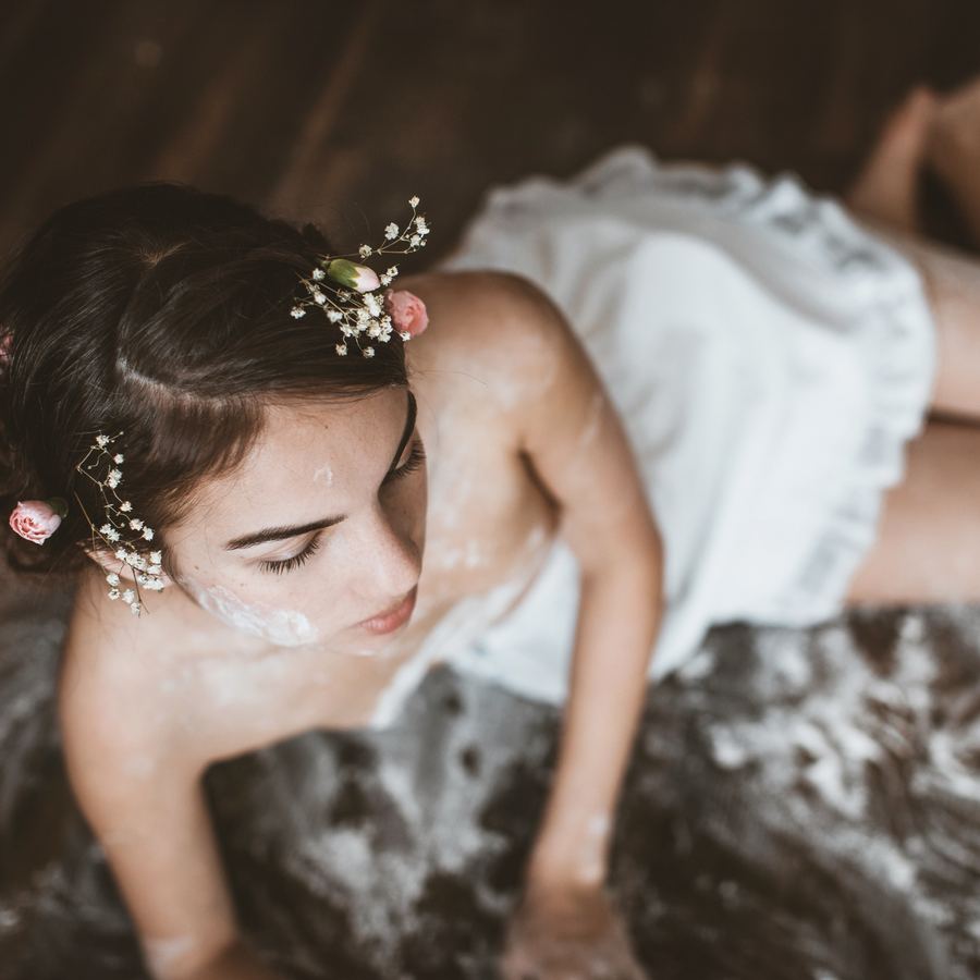 Fine-art boudoir portrait from above, flowers in her hair and flour on her skin